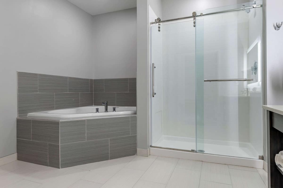 Een moderne badkamer met een douche met glazen wand, een vrijstaand bad en grijze betegelde wanden.