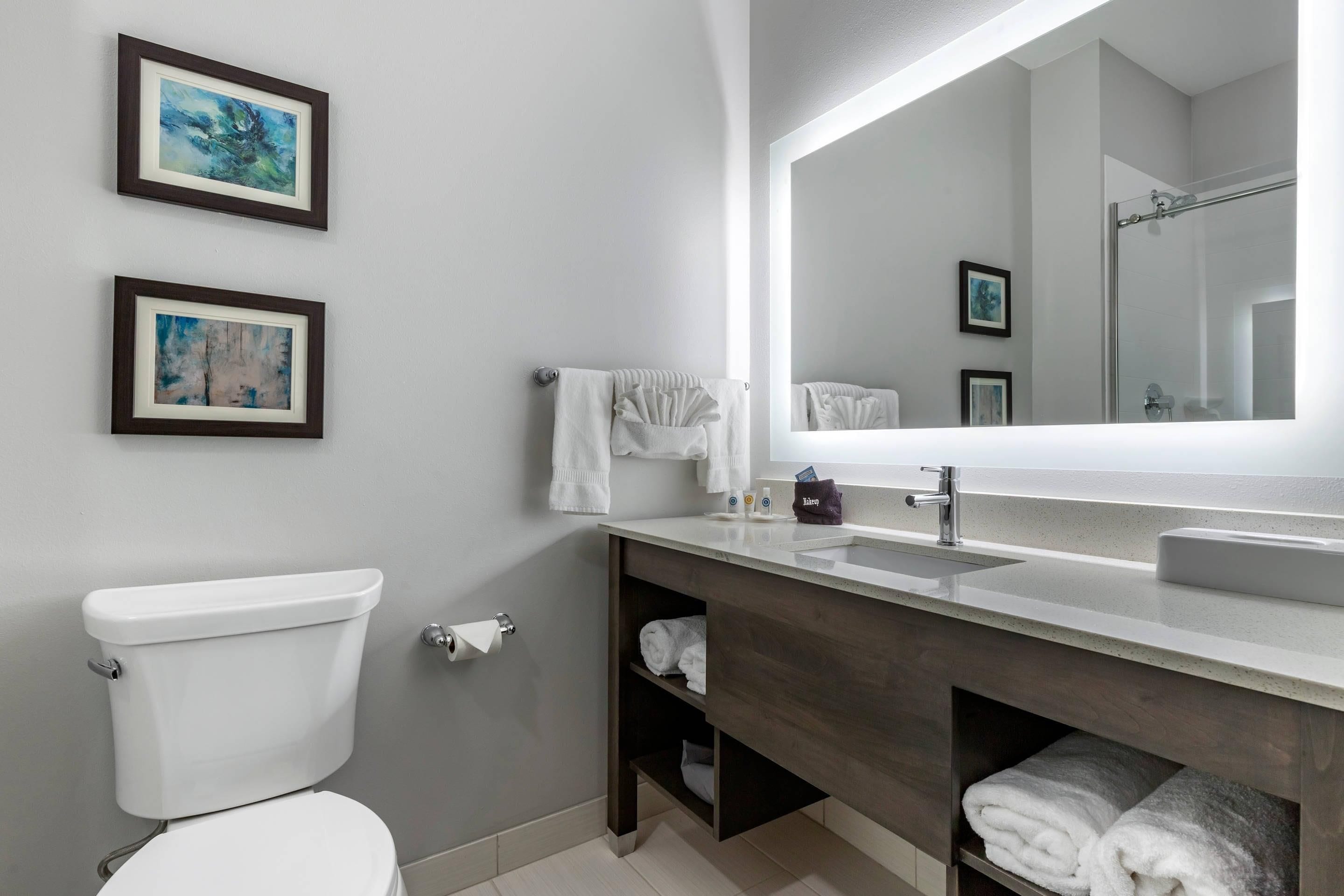 Un baño moderno con inodoro, lavamanos y espejo. Hay dos cuadros enmarcados en la pared.