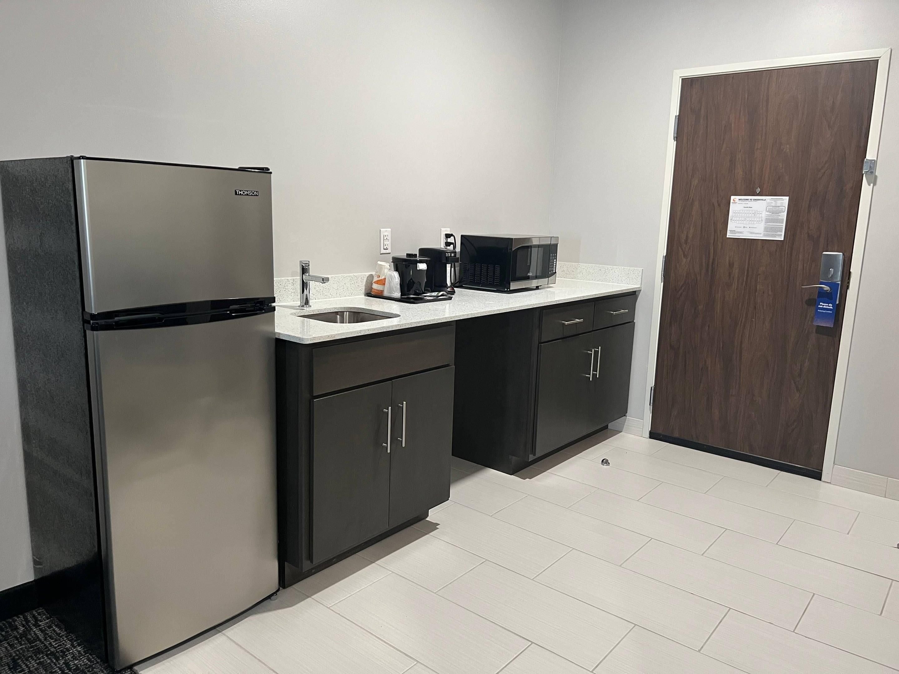 A compact kitchen with a stainless steel refrigerator, a microwave, and a coffee maker on the countertop.