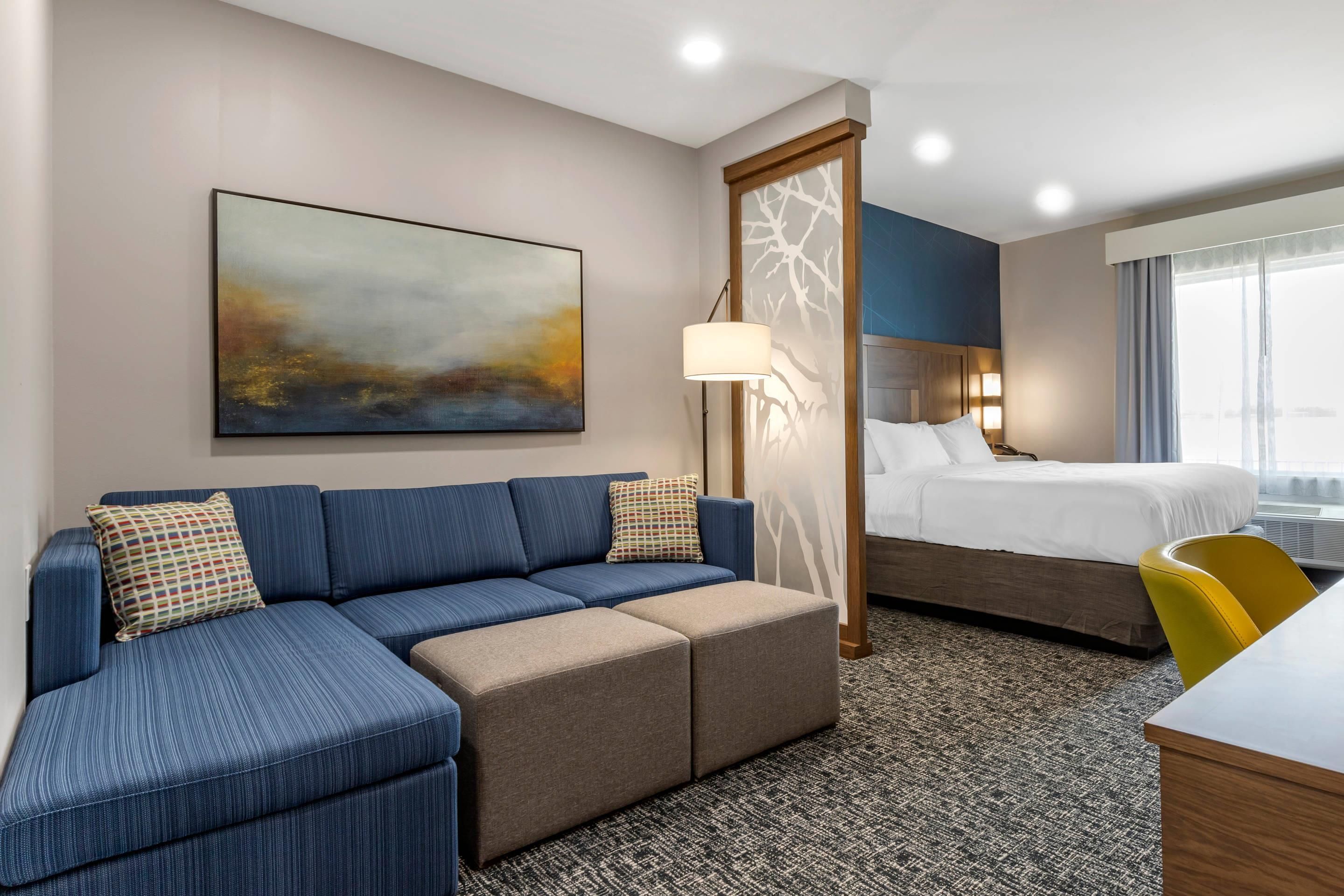 A hotel room with a blue sofa, a bed, a desk, and a large window.