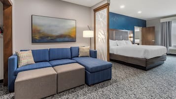 A hotel room with a blue sofa, a bed, a large abstract painting, and a patterned carpet.