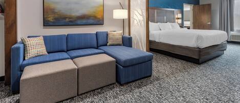 Habitación de hotel con un sofá azul, una cama, un cuadro abstracto grande y una alfombra estampada.