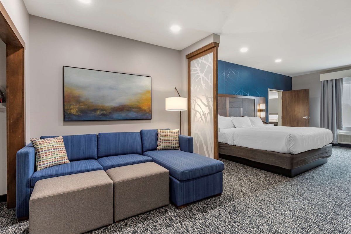 Een moderne hotelkamer met een hoekbank, een bed en een groot abstract schilderij aan de muur.