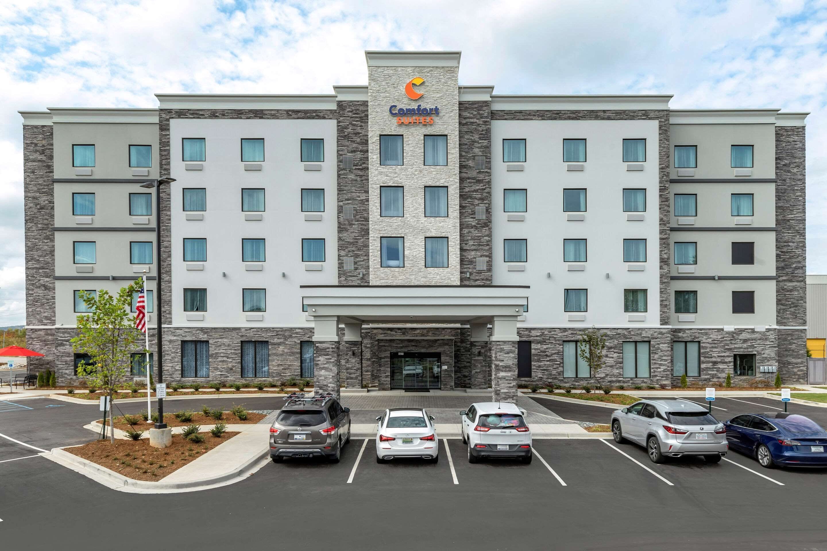 Un hôtel Comfort Suites au design moderne, doté d’une entrée principale, de nombreux espaces de stationnement et d’un espace paysager agrémenté de petits arbres.