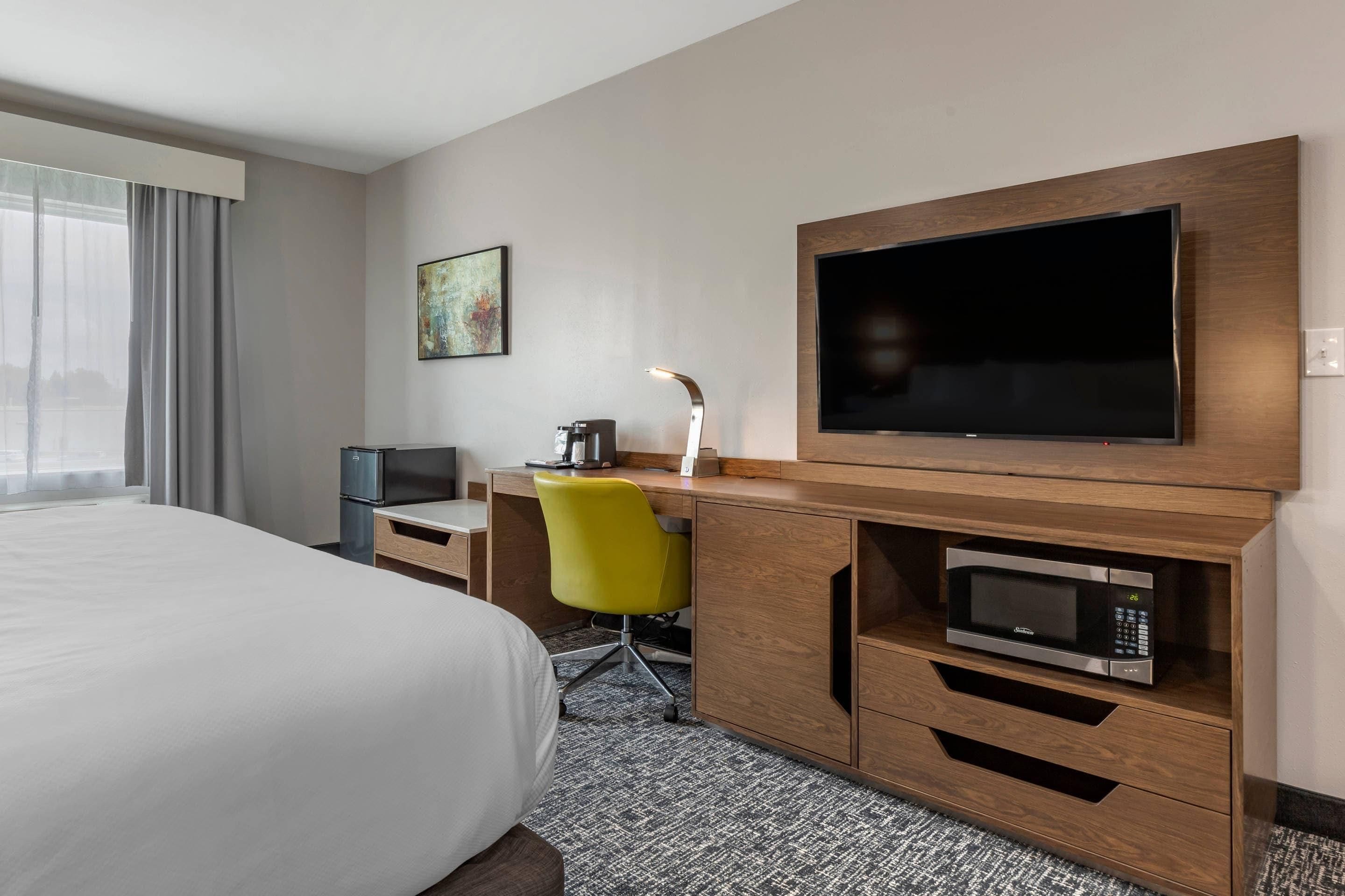 A hotel room with a bed, a desk with a computer, a television, a microwave, and a chair.