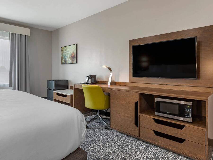 A hotel room with a bed, a desk with a computer, a television, a microwave, and a chair.