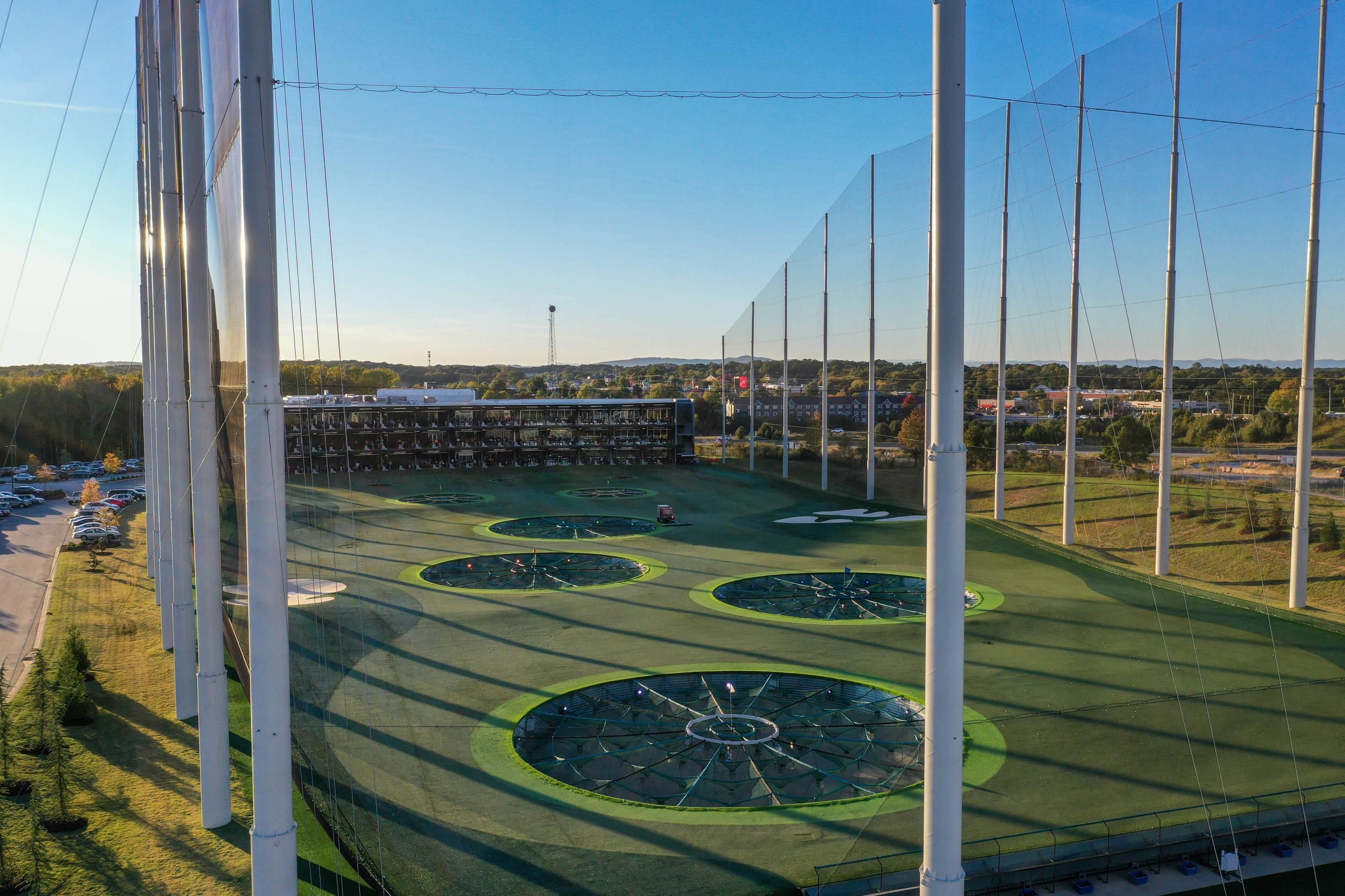 A sports field with multiple circular green areas, surrounded by tall white poles, and a building with a flat roof in the background.
