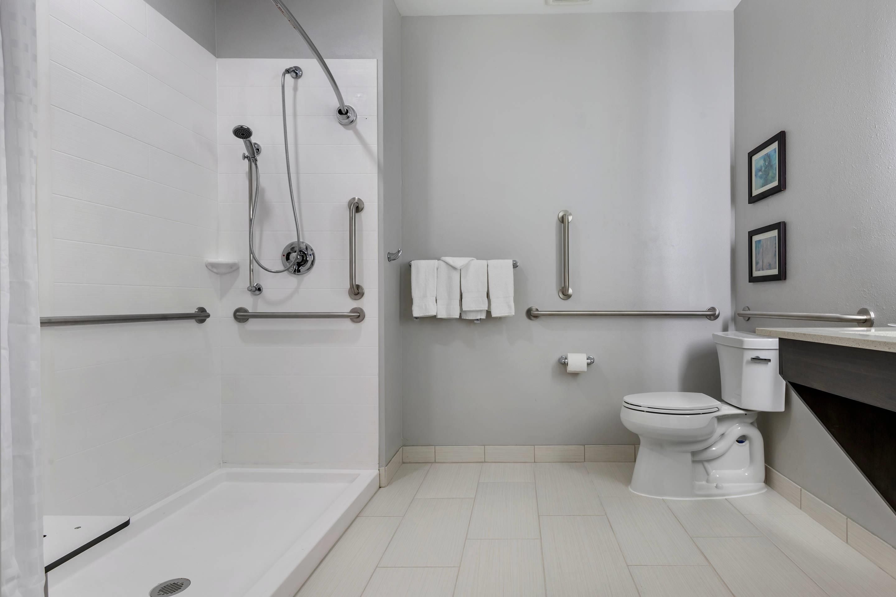 Un baño moderno con cabina de ducha, barras de apoyo, inodoro y lavabo.