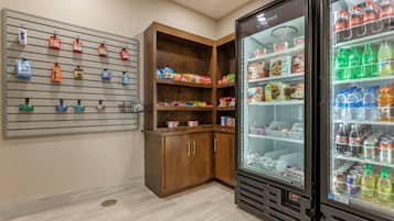 Habitación de hotel con minibar, refrigerador lleno de bebidas y estante con aperitivos y artículos de aseo.