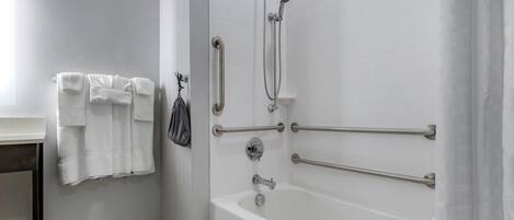 Un baño con bañera, barras de apoyo, un perchero y un cabezal de ducha.