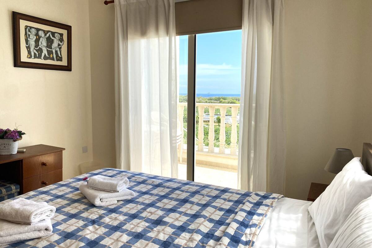 A hotel room with a bed, a nightstand, a framed picture, and a balcony with a view.
