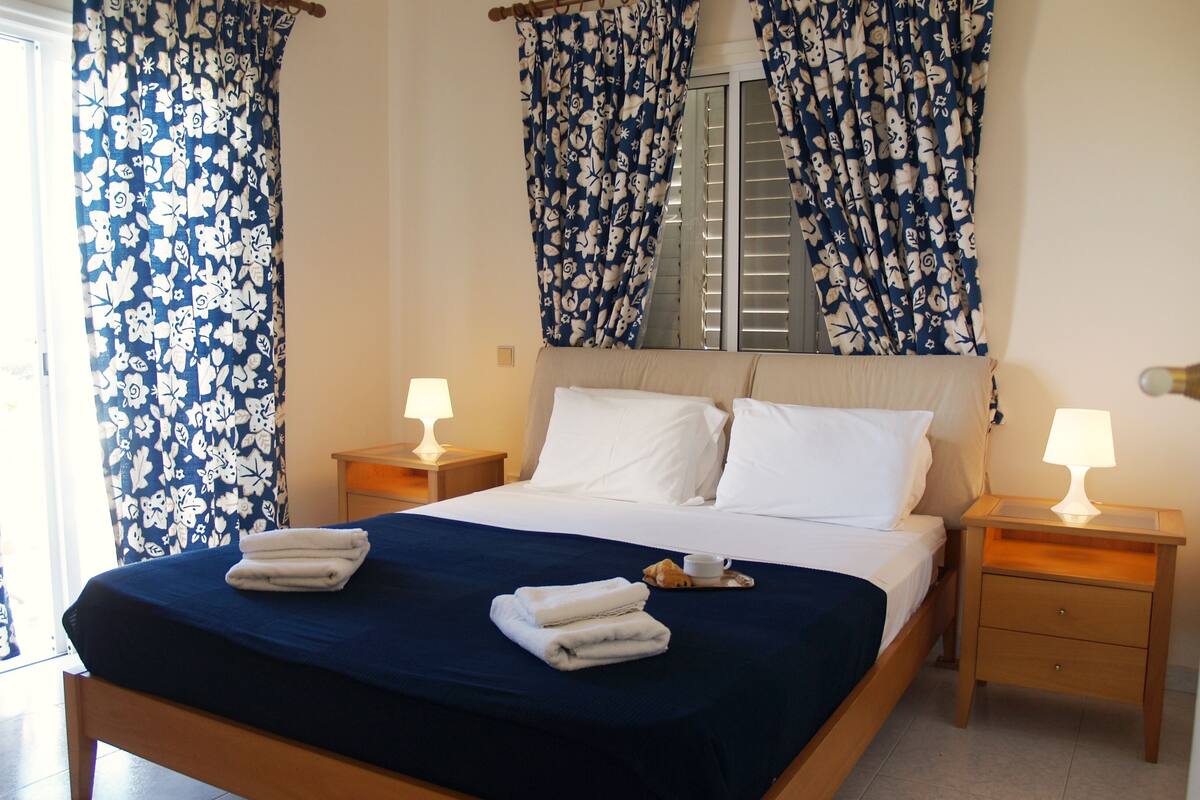 A neatly made bed with white linens, two bedside tables with lamps, and a window with curtains.