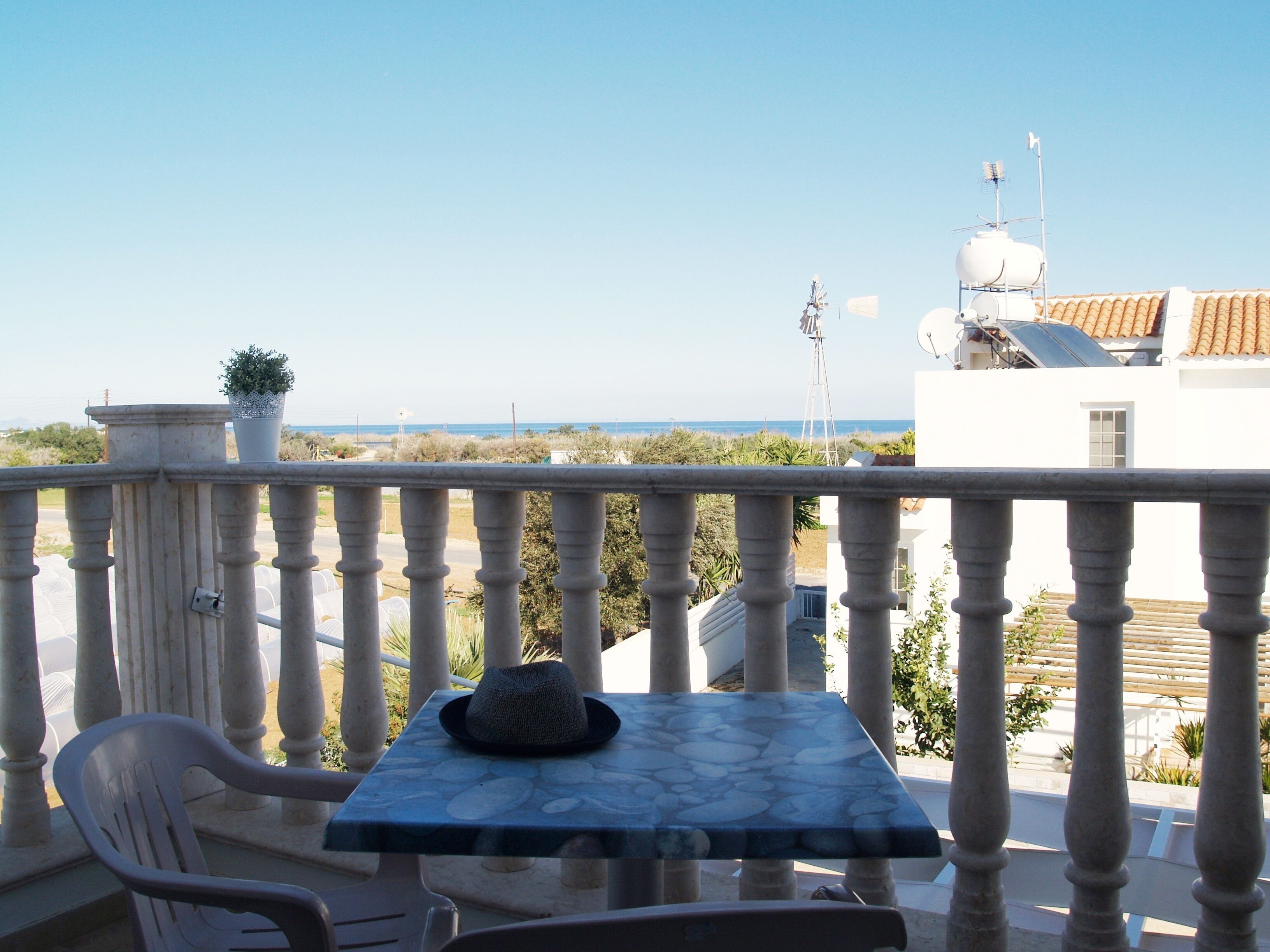 Un balcone con tavolo e sedie, affaccia su una vista costiera con edifici e un mulino a vento in lontananza.