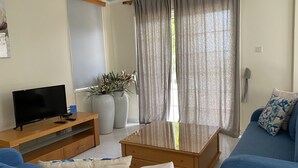 A living room with a flat-screen TV, a wooden coffee table, a blue sofa, and a glass-top coffee table. - Villa Ithaca Protaras (Paralimni)
