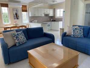 Una sala de estar moderna con dos sofás azules, una mesa de centro de vidrio y un comedor con sillas de madera y una pequeña mesa.