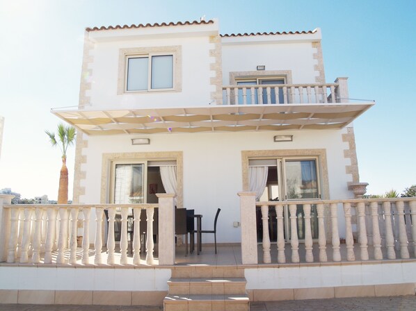 A two-story building with a balcony, a covered patio, and a staircase leading to the entrance. - Villa Ithaca Protaras (Paralimni)