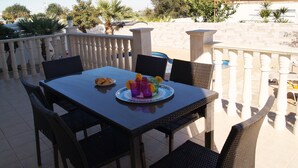 An outdoor patio with a table set for two, surrounded by wicker chairs. - Villa Ithaca Protaras (Paralimni)