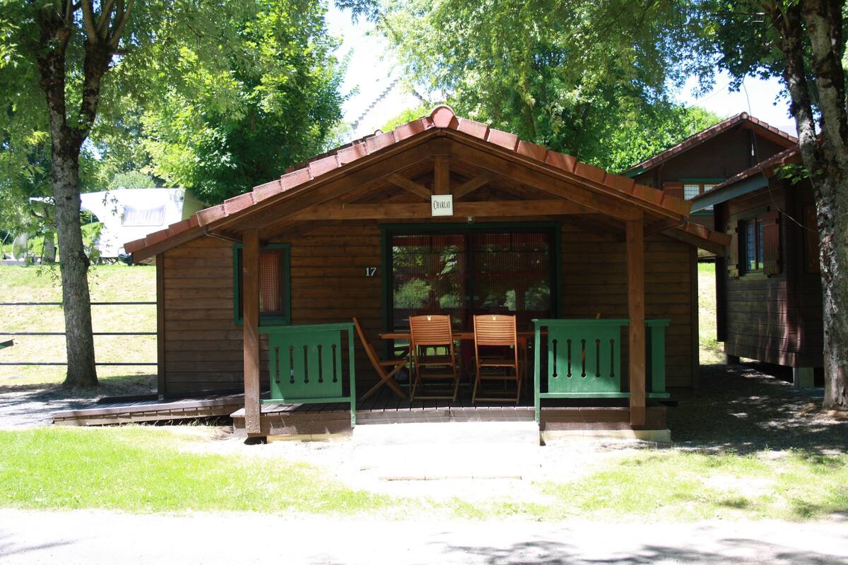A wooden cabin with a porch, two wooden chairs, and a table.