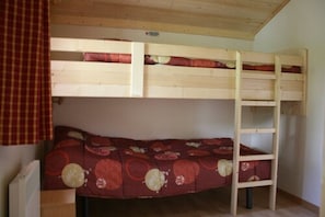 A bunk bed with a lower bunk and a ladder, a mattress with a red floral pattern, and a wooden ceiling. - Camping les étoiles (Saint-Sornin-Lavolps)