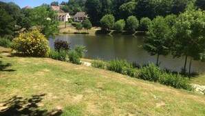 A lakeside view with a grassy area, trees, and a building in the background.