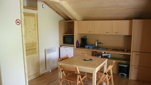 A compact kitchen with wooden cabinets, a microwave, a refrigerator, and a dining table with chairs.