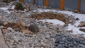 Un giardino con muro in pietra, ghiaia e chiazze di neve.
