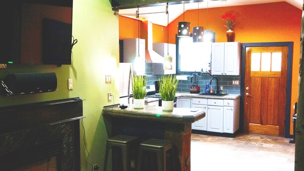 Cucina con angolo bar, mobili bianchi, una porta in legno e una TV a parete.