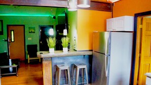 Una cucina con frigorifero in acciaio inox, bancone in legno, due sgabelli e una pianta in vaso.