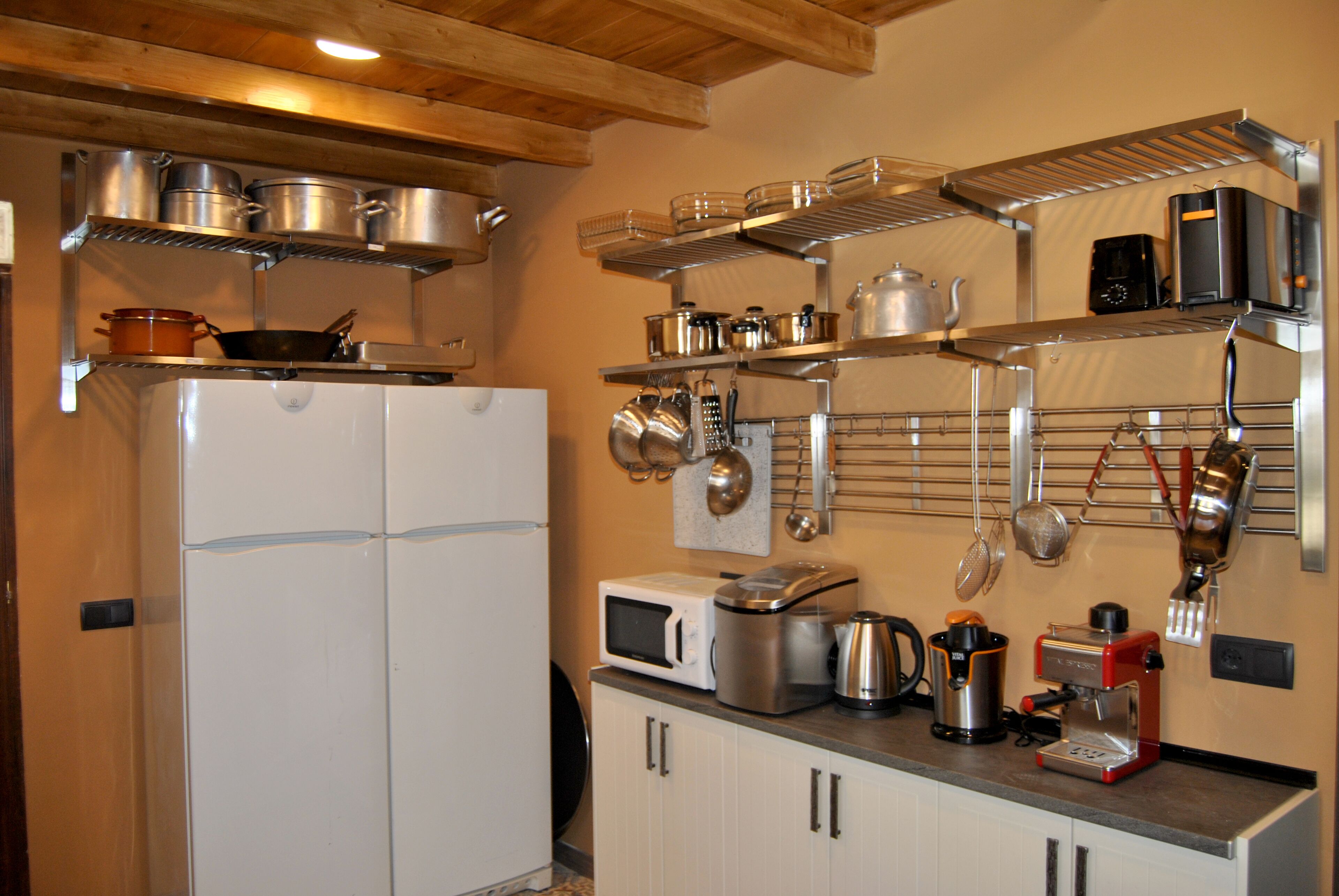 Een keuken met witte kastjes, een magnetron, een koffiezetapparaat en diverse pannen en potten op planken.