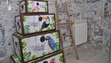 A set of three stacked suitcases with tropical-themed artwork, a wooden ladder, and a radiator on a tiled wall.