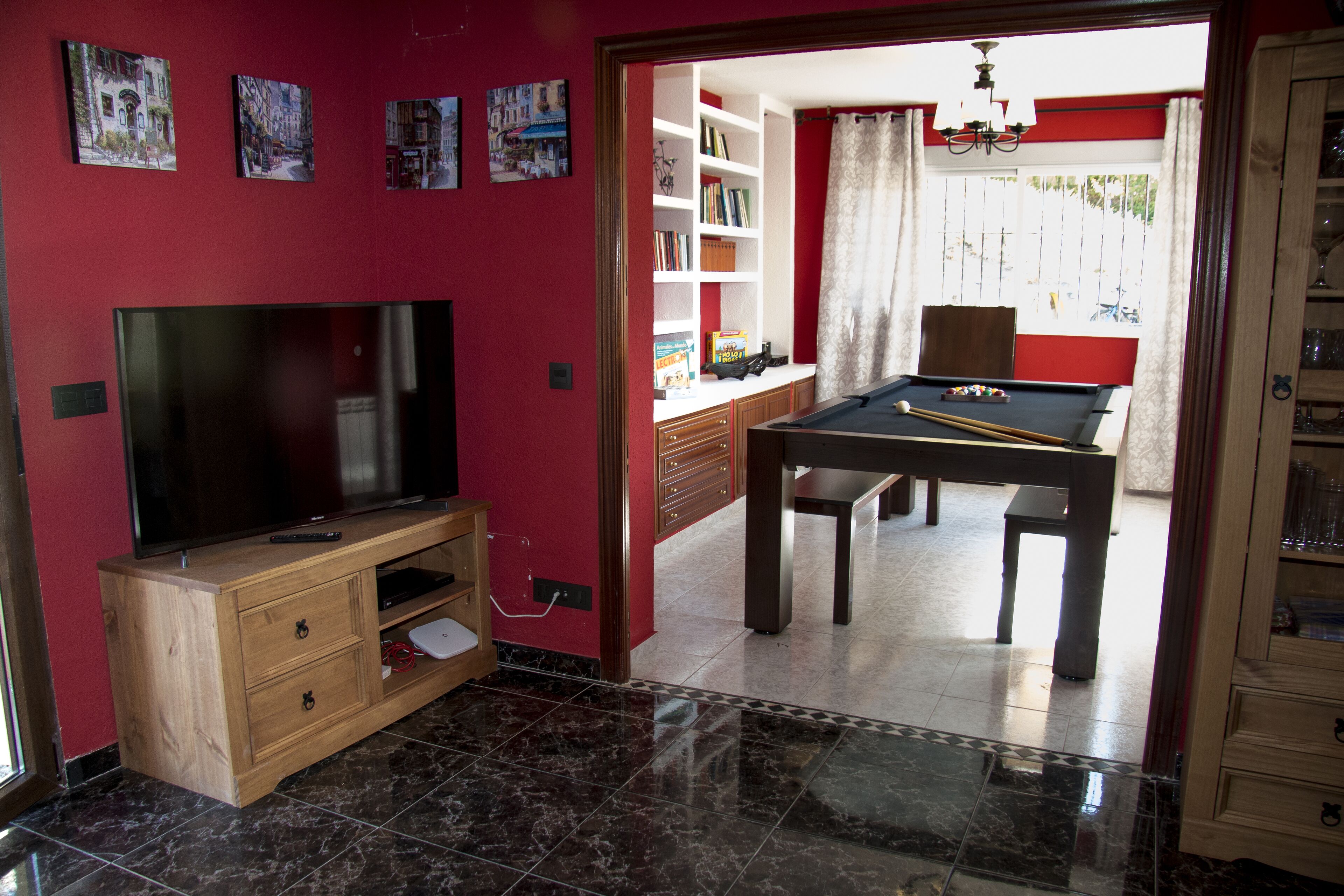 Une pièce avec un téléviseur posé sur un meuble en bois, une table de billard et une bibliothèque remplie de livres.