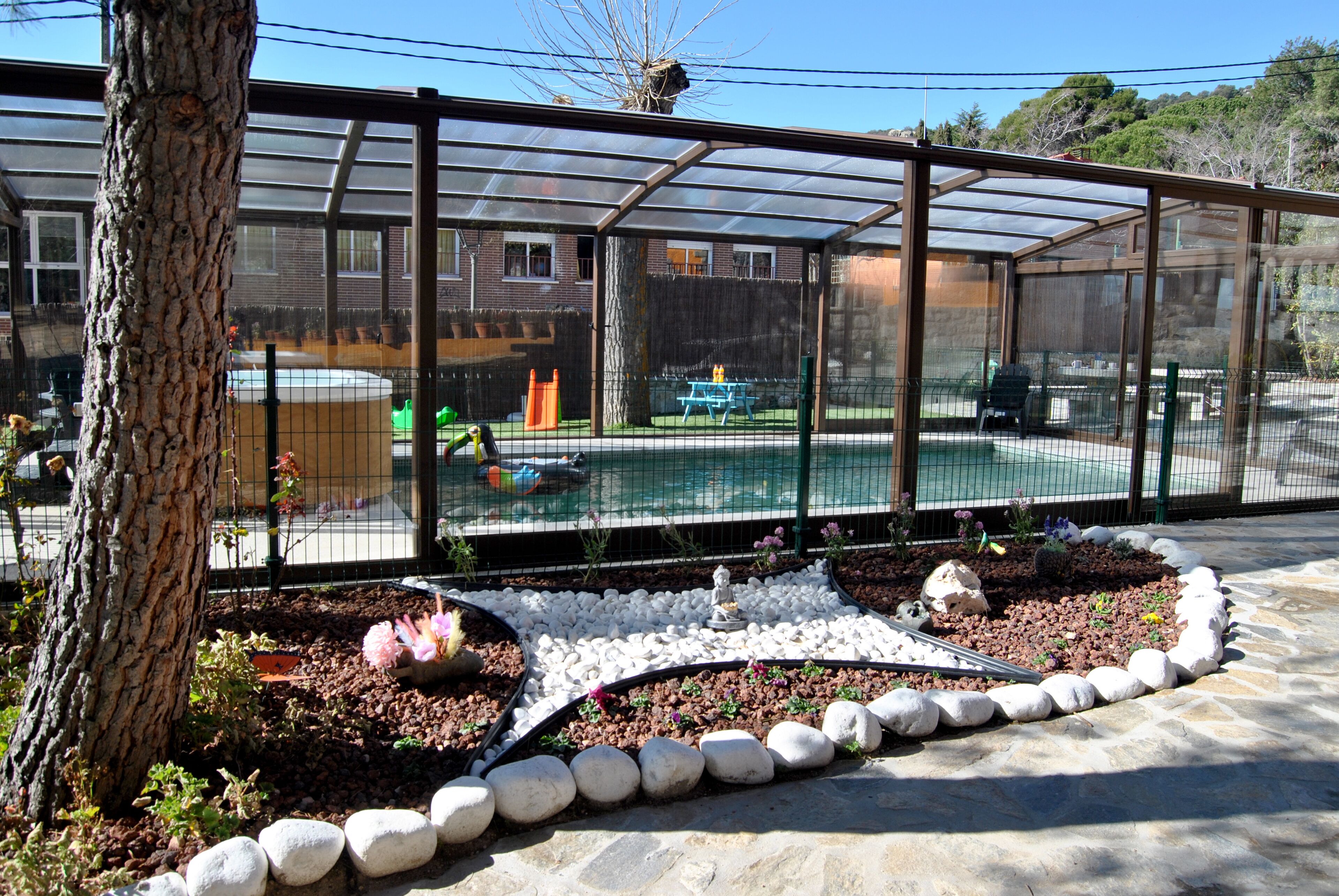 Una estructura de serra amb teulada transparent, envoltada d'un jardí de pedres blanques i plantes.