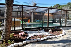 A greenhouse structure with a transparent roof, surrounded by a garden with white pebbles and plants. - Casas Rurales Collarubio (Collado Mediano)