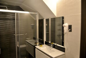 A modern bathroom with a glass shower enclosure, a white sink, and a hairdryer mounted on the wall. - Casas Rurales Collarubio (Collado Mediano)