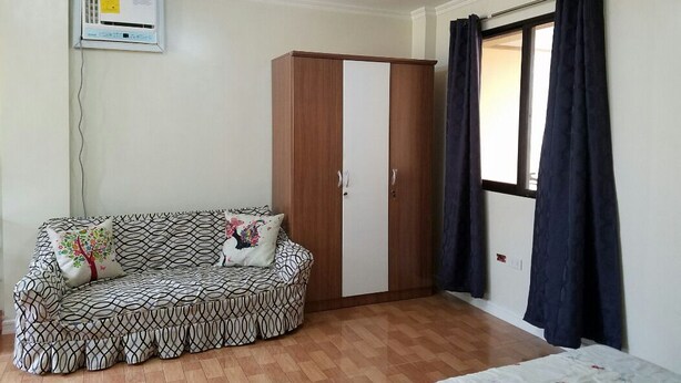 Ein Zimmer mit Holzschrank, gepunktetem Sofa, Deckenventilator und einem fenster mit Vorhängen.