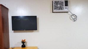 Ein Zimmer mit einem Holztisch, zwei Hocker, einem Fernseher und einer Klimaanlage.