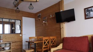 Un intérieur en bois comprenant une table à manger, des chaises, un canapé, un téléviseur fixé au mur et un miroir.