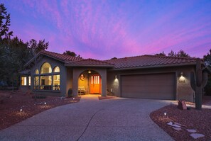 Enter a welcoming home with a large entrance, glass door, and small patio area surrounded by a beautifully landscaped garden.