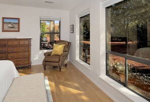 Enjoy a peaceful retreat with a view of the wooded area from the large window, a comfortable armchair, and a dresser for your belongings.
