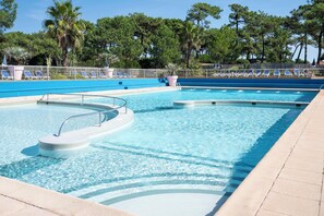 Une piscine avec un plongeoir, des chaises longues et un espace clos entouré d’arbres en arrière-plan.