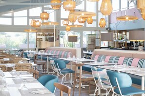 A restaurant with high ceilings, wicker pendant lighting, and a mix of blue and wooden chairs. Tables are set with white tablecloths and glassware. - Belambra Clubs Capbreton - Les Vignes (Capbreton)