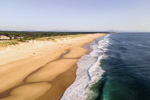 Una playa extensa con olas suaves, cielo despejado y montañas a lo lejos.