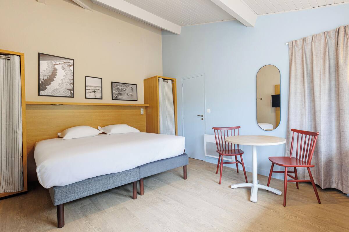 Ein Hotelzimmer mit einem Bett, einem kleinen Tisch, zwei Stühlen, einem Spiegel und Bildern an der Wand.