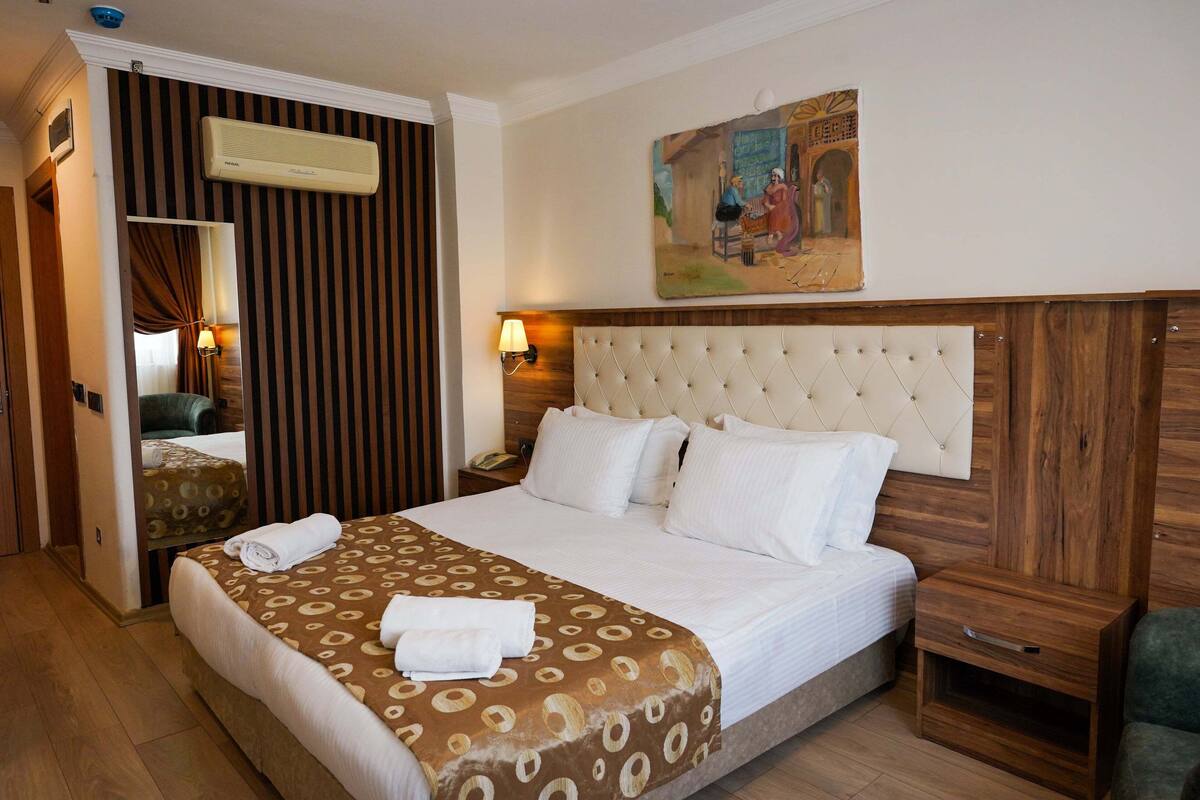 A hotel room with a large bed, a wooden headboard, a nightstand, a lamp, and a painting on the wall.