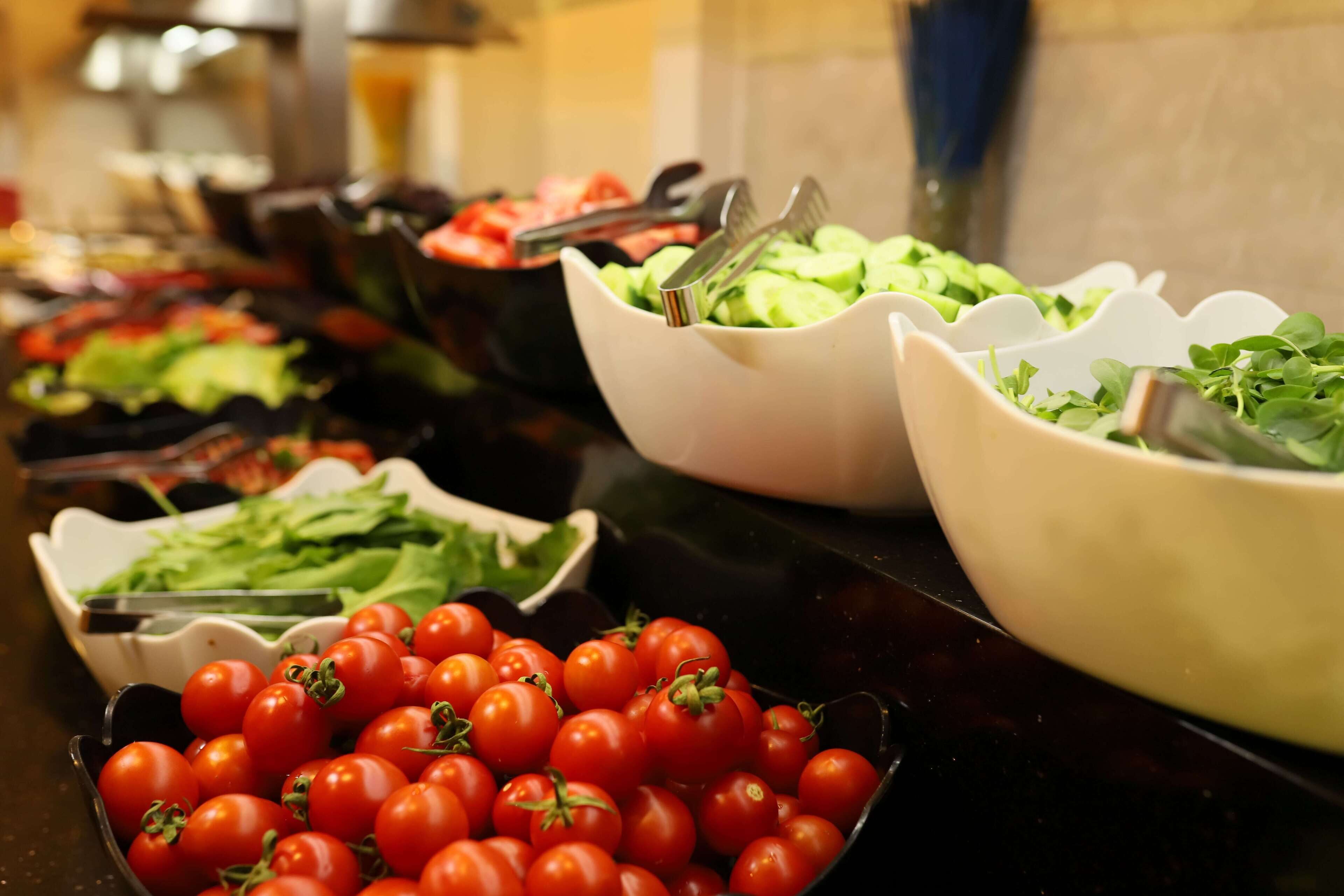 Un bufé con diversos alimentos, incluyendo tomates, lechuga y otras verduras.