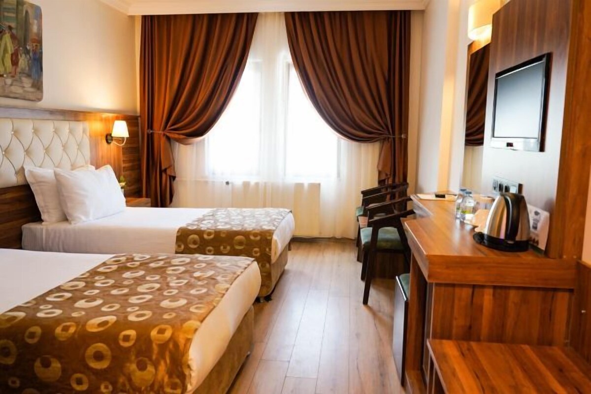Habitación de hotel con dos camas, un escritorio, un televisor y una ventana con cortinas.