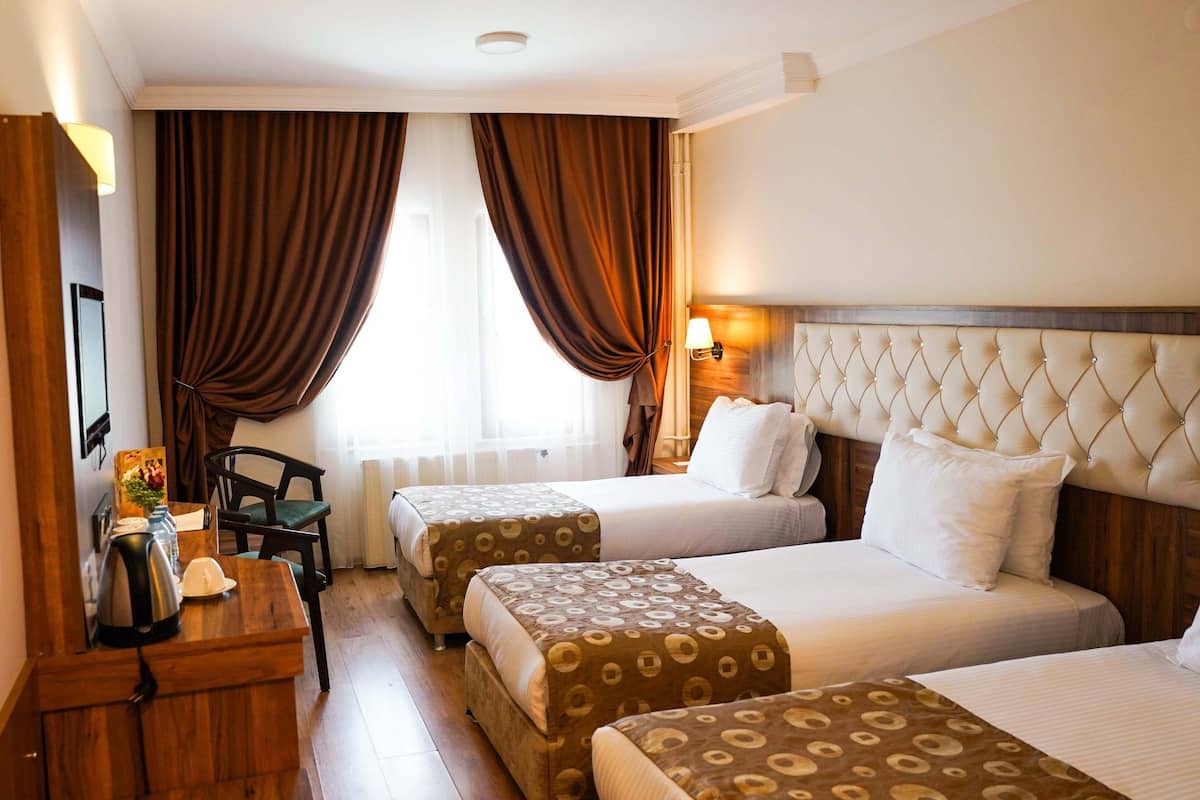 A hotel room with two beds, a wooden desk, a chair, and a window with curtains.