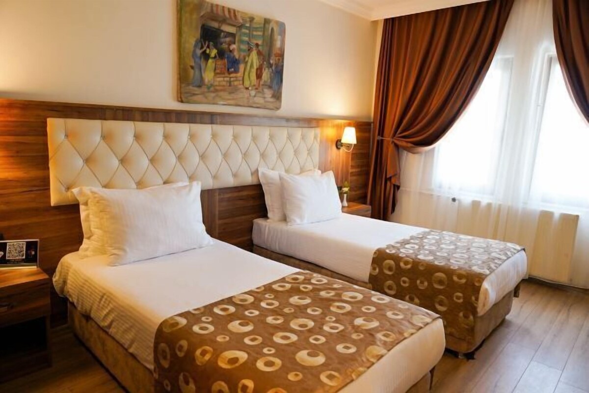 A hotel room with two beds, a wooden headboard, a painting on the wall, and a window with curtains.