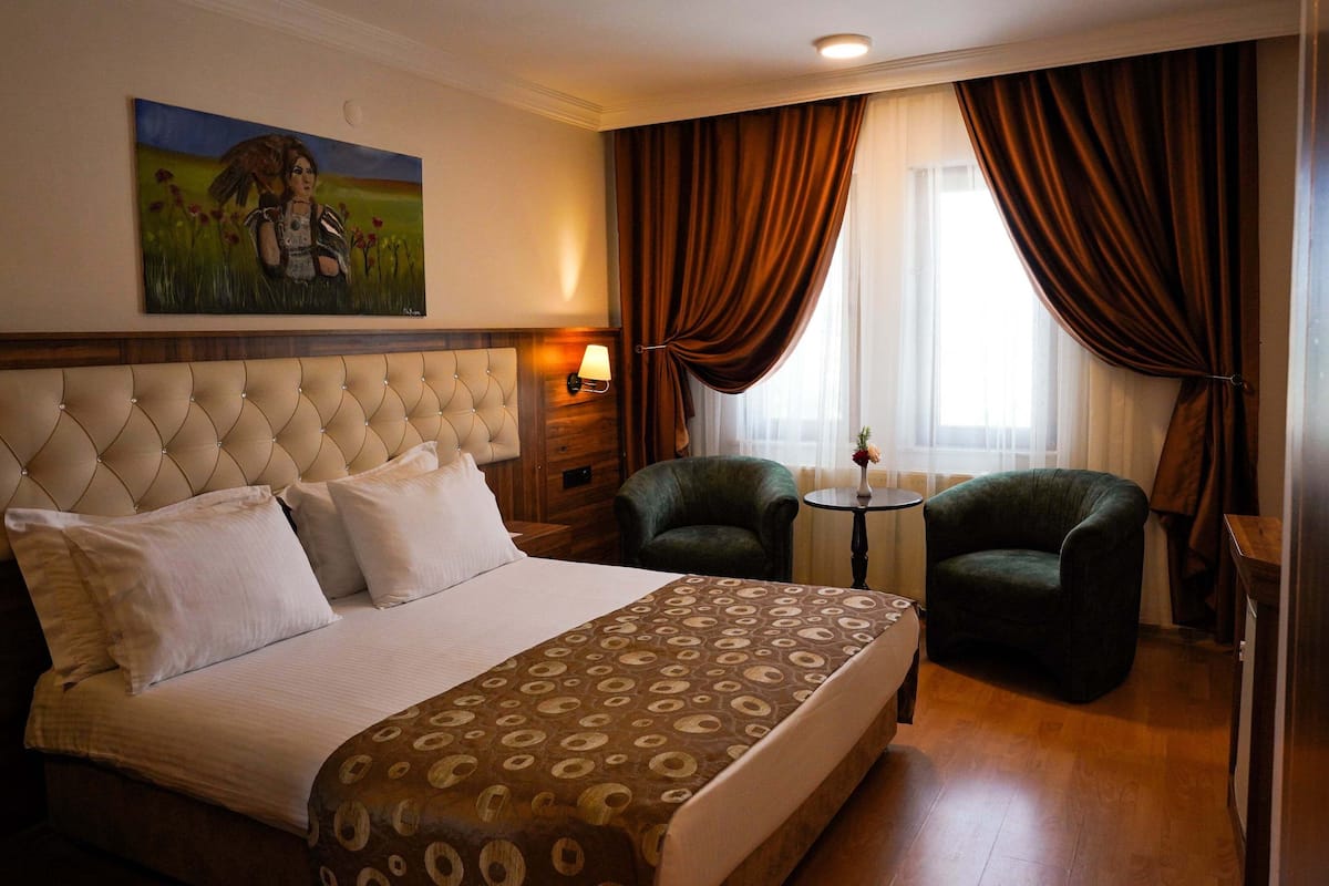 A hotel room with a large bed, two armchairs, a small table, and a painting on the wall.