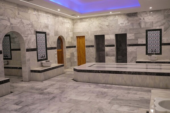 Un baño moderno con suelo de mármol, una bañera grande y varios lavamanos.